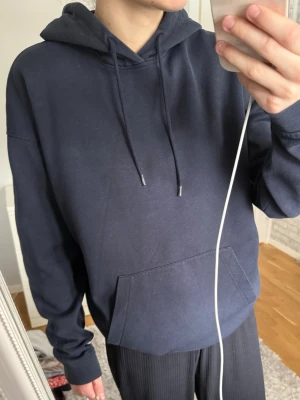 Mörkblå hoodie från Jack & Jones - Mörkblå hoodie från Jack & Jones med klassisk känguruficka och dragsko i huvan. Mjuk insida och ribbade muddar vid ärmslut och nederkant. Perfekt för en avslappnad och stilren look.