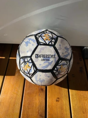 4Freestyle Control Fotboll - Säljer en 4Freestyle Control boll, perfekt för freestyle och trick. Bollen är vit med blå och grå kamouflagemönster, svarta kanter och guldiga stjärndetaljer. Tillverkad i slitstarkt material för bra grepp och kontroll. Grym för dig som vill ta dina skills till nästa nivå.
