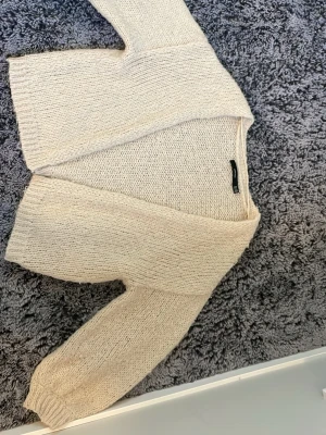 Beige stickad kofta från Gina Tricot - Mysig beige stickad kofta från Gina Tricot med öppen front och långa ärmar. Koftan har en avslappnad passform och är gjord i ett mjukt, grovstickat material som passar perfekt för lager på lager. Enkel och stilren design.