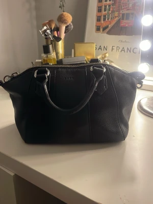 Svart handväska från Esprit i skinn - Pris kan diskuteras ❤️plus man får med ett långt band också❤️Snygg svart handväska från Esprit i äkta skinn med grov struktur. Väskan har två handtag och en robust dragkedja upptill. Perfekt storlek för att bära med sig det viktigaste och passar till många olika stilar. Den har tappat lite färg på låset och lite skavanker.