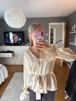 Beige omlottblus från Missay - Snygg beige omlottblus från Missay med långärmad design och knytband i midjan. Blusen har en v-ringning och är gjord i ett glansigt, mjukt material. Använd två gånger!