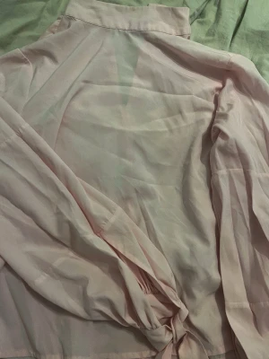 Ljusrosa blus med knytärm - Snygg ljusrosa blus med klassisk krage och långa ärmar som avslutas med trendiga knytband vid handlederna. Blusen har en rak passform och är tillverkad i ett tunt, mjukt tyg som ger en luftig känsla.