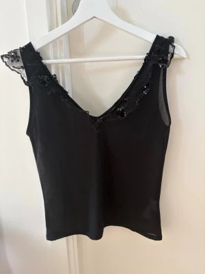 Svart linnetopp med spets och paljetter - Snygg svart linnetopp med v-ringning och spetsdetaljer vid axlarna. Toppen har paljetter längs spetsen för extra bling🖤
