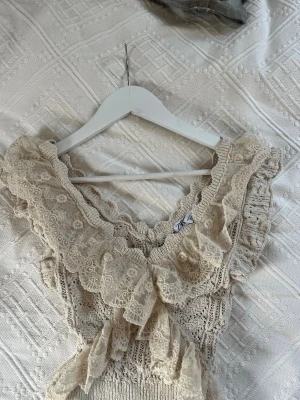 Beige spetsvolang topp från Zara - Säljer en beige topp från Zara med v-ringning och breda volanger i spets. Toppen är stickad med fina detaljer och har en croppad passform. Perfekt för dig som gillar romantisk och feminin stil.