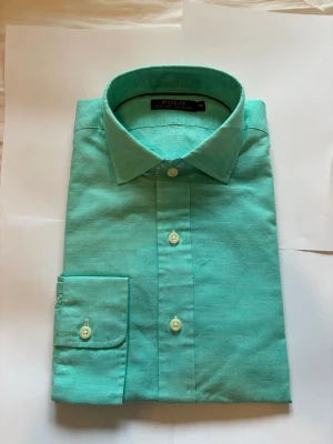 Turkos skjorta från Polo Ralph Lauren - Turkos linnen skjorta från Polo Ralph Lauren helt oanvänd men skyddet för kragen kvar. Köpt på en sample sale för polo så den säljs ej i butik längre och är väldigt sällsynt