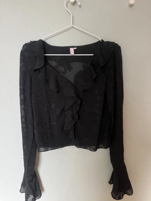 Svart blus - Svart, lite genomskinlig blus från Nelly med volanger och mönster! Använd fåtal gånger så i mycket fint skick!