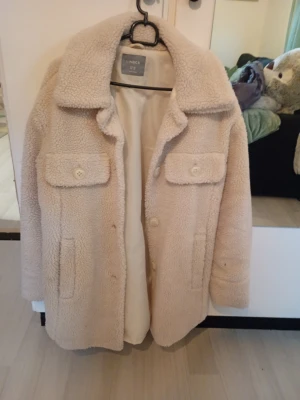 Beige teddyjacka från Lindex - Supermjuk och fluffig teddyjacka i beige från Lindex. Jackan har stora knappar framtill, två bröstfickor med lock och en bred krage. Perfekt oversized look och riktigt mysigt material som håller dig varm under kalla dagar.