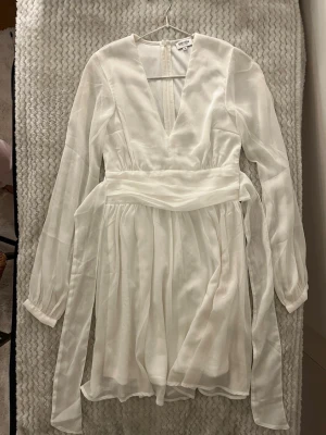 Vit omlottklänning från Bik Bok - Säljer en vit kortklänning från Bubblerum med v-ringning, långärmad design och omlott med knytband i midjan. Klänningen är gjord i ett lätt och luftigt material som ger en flowy känsla. Perfekt för dig som vill ha en stilren och fräsch look.
