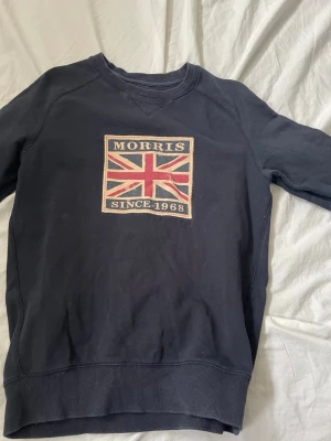 Mörkblå sweatshirt från Morris - Mörkblå sweatshirt från Morris med Union Jack-flagga och texten 'Morris Since 1968' på bröstet. Tröjan har rund halsringning och långa ärmar. Perfekt för en avslappnad och stilren look.