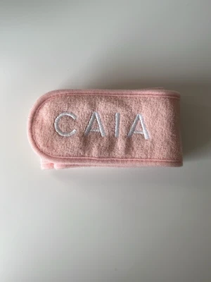 Rosa hårband från CAIA - Säljer ett mjukt och stretchigt rosa hårband från CAIA med broderad logga i vitt. Perfekt för att hålla håret borta vid sminkning eller hudvård. Tillverkat i ett skönt frottéliknande material och har en enkel, stilren design. I nytt skick.