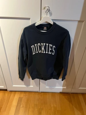 Mörkblå Dickies sweatshirt - Mörkblå sweatshirt från Dickies med vit broderad logga över bröstet. Klassisk rund halsringning, ribbade muddar vid ärmslut och nederkant. Perfekt för en avslappnad och stilren look.