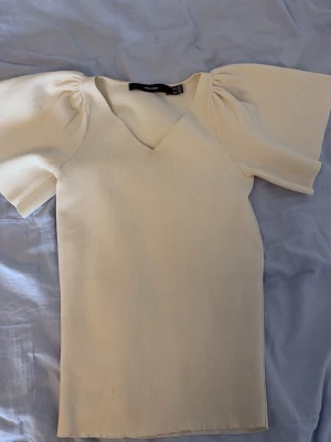 Ljusbeige topp med puffärm - Supersnygg ljusbeige topp från Vero Moda med puffiga korta ärmar. Toppen är i mjukt stretchigt material som sitter bekvämt. Perfekt för dig som vill ha en enkel men stilren topp med lite extra volym på axlarna. Toppen är använd men i mycket bra skick.