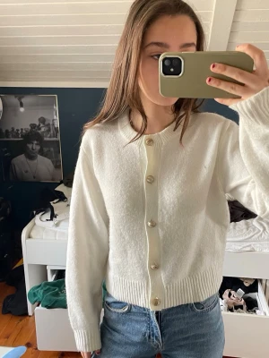 Vit kofta med pärlknappar - Säljer en vit, mjuk kofta med ribbade muddar och snygga pärlknappar framtill. Koftan har rund hals och långa ärmar, perfekt att slänga över en t-shirt eller topp. Passar dig som gillar en clean och stilren look.