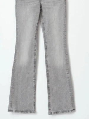 Grå bootcut jeans med fickdetaljer - Säljer ett par grå bootcut jeans med snygg tvätt och dekorativa fickor bak med lock och knapp. Jeansen har utsvängda ben och klassisk femficksmodell. Perfekta för dig som gillar retrovibbar och vill ha en avslappnad men trendig look.