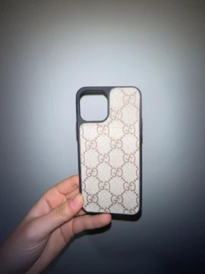Mobilskal med GG-mönster - Snyggt mobilskal med klassiskt beige och brunt GG-mönster. Skalet har svart ram och är gjort i ett tåligt material som skyddar mobilen. Passar perfekt för dig som vill ha en lyxig och trendig look på din telefon. 