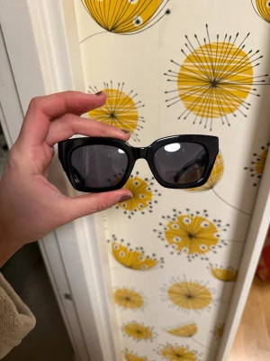 Svarta solglasögon Tommy Hilfiger - Snygga svarta solglasögon från Tommy Hilfiger med breda bågar och mörka glas. Klassisk rektangulär form och guldfärgad TH-logga på sidan. Perfekta för att lyfta din stil med en cool touch.