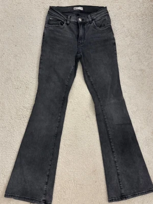 Mörkgråa bootcut jeans från Gina Tricot - Snygga mörkgråa bootcut jeans från Gina Tricot med klassisk femficksmodell och hög midja. Jeansen har utsvängda ben och är tillverkade i stretchigt denimtyg för en bekväm passform. Perfekta för en trendig och avslappnad look.