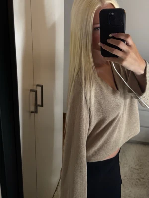 Beige croppad stickad topp - Säljer en beige croppad stickad topp med v-ringning och långa ärmar. Perfekt för dig som gillar en avslappnad och trendig stil. Toppen har en loose passform och är riktigt mjuk och skön.