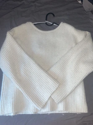 Vit stickad tröja med rosett i ryggen - Superfin vit stickad tröja med ribbad struktur och lång ärm. Tröjan har en snygg öppen rygg med en bred rosett som knyts upptill.