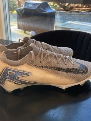 Nike Mercurial Superfly fotbollsskor - Säljer ett par Nike Mercurial Superfly Snowpack edition  fotbollsskor i beige och grått med svart Swoosh och blå detalj på sidan. Skorna har snörning, låg profil och mönstrad sula för bra grepp på planen. Ovandelen är i syntetmaterial för lätt vikt och bra bollkontroll.