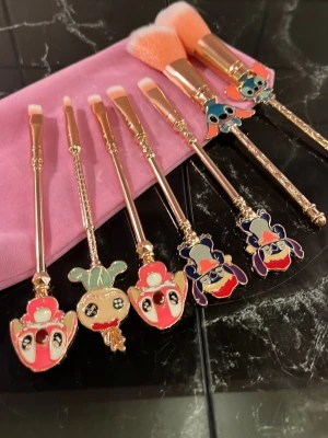 Söta sminkborstar Stitch - Set med sju sminkborstar i roséguld med färgglada, tecknade figurer på skaften. Borstarna har mjuka, ljusrosa borst och detaljerade handtag i metall. Perfekt för dig som gillar unika och lekfulla sminkverktyg. Levereras med en rosa tygpåse.
