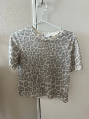 Leopardmönstrad topp från Zara - Kortärmad topp från Zara med grått leopardmönster på ljus botten. Tunn och lätt genomskinlig kvalitet med rund halsringning och normal passform. Perfekt för dig som gillar djurmönstrat och vill ha en trendig look.