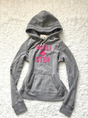 Grå hoodie från Hollister med rosa tryck - Grå hoodie från Hollister i storlek M