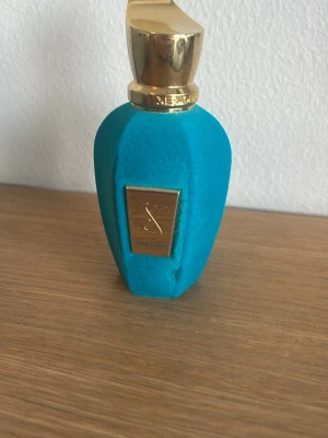 Xerjoff erba pura  - Unik parfymflaska från xerjoff i en snygg turkos sammet med guldfärgat lock och metallskylt framtill. Flaskan har en elegant, modern form och känns riktigt lyxig. Perfekt för dig som vill ha något som sticker ut på parfymhyllan.