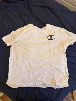 Vit Champion t-shirt med logga - Vit t-shirt från Champion med klassisk logga på bröstet och ett broderat Champion-märke på ärmen. T-shirten har rund hals och korta ärmar, perfekt för en avslappnad och sportig stil.