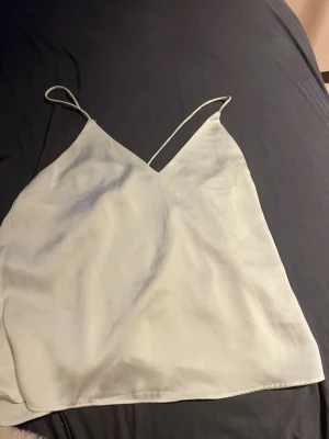 Vit linnetopp med tunna axelband - Snygg vit linnetopp med tunna axelband och v-ringad hals. Toppen har en enkel och stilren design, perfekt att matcha med jeans eller kjol. Materialet känns lätt och svalt, vilket gör den grym för varmare dagar.