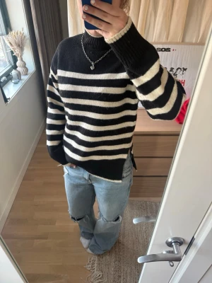 Svartvit randig stickad tröja - Säljer en svart och vit stickad tröja med breda horisontella ränder. Tröjan har hög hals, långa ärmar och ribbstickade muddar. Oversized passform och mjukt material, perfekt för lager-på-lager-stil.