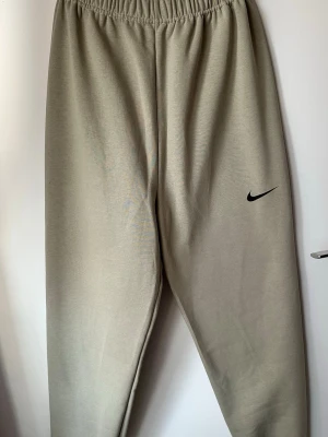 Beige mjukisbyxor från Nike xs-s - det finns inga fickor!Säljer ett par beige mjukisbyxor från Nike med klassisk svart Swoosh-logga på benet. Byxorna har resår i midjan och är gjorda i mjukt bomullsmaterial för maximal komfort. Perfekta för chill dagar eller när du vill ha en avslappnad stil.