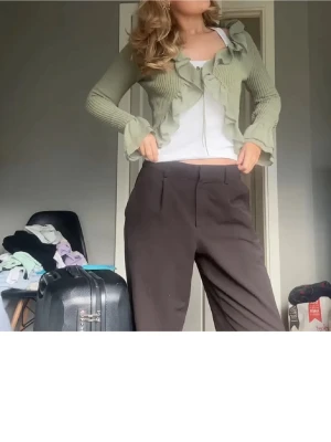 Grön volangstickad kofta från Zara - Trendig ljusgrön stickad kofta från Zara med volangdetaljer längs kanterna och vid ärmsluten. Kortare modell med knytning framtill och ribbad struktur. Perfekt för att lyfta din outfit med en söt och unik touch.