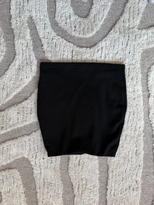 Svart tight kortkjol i strukturtyg - En svart, tight kortkjol i ett strukturerat tyg med diskret mönster. Kjolen har en enkel och stilren design utan synliga detaljer och passar perfekt till många olika outfits. Knappt använd. 