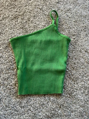 Grön ribbad asymmetrisk topp - Snygg grön ribbad topp med oneshoulder-design och smal axelrem. Superfin i sommar!! Använd fåtal gånger