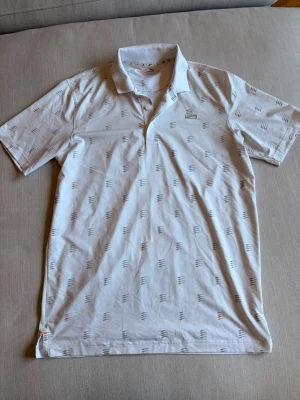 Golftröja puma - Vit golfpiké från Puma med mönster i grått och orange. Storlek S men passar även M.