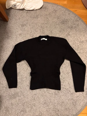 Svart stickad tröja från Zara - En svart, figurnära stickad tröja från Zara med rund halsringning och långa ärmar. Tröjan har en enkel och stilren design, perfekt att matcha med olika outfits. Materialet känns mjukt och stretchigt för en bekväm passform.