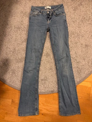 Blå bootcut jeans från Zara - Snygga blå bootcut jeans från Zara med klassisk femficksdesign och låg midja. Jeansen har en lätt tvättad look och är tillverkade i ett mjukt denimtyg som ger en bekväm passform. Perfekta för dig som gillar en tidlös och avslappnad stil.