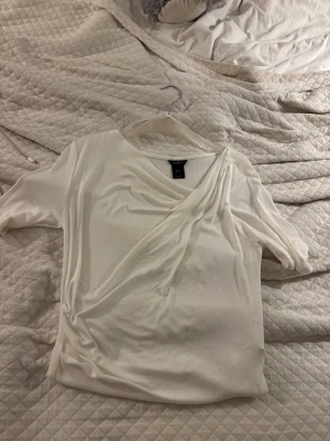 Vit omlottopp från Lindex - Snygg vit omlottopp från Lindex i mjukt material. Toppen har korta ärmar och ett omlottparti framtill som ger en stilren look. Perfekt att matcha med jeans eller kjol för en trendig outfit.