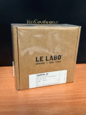 Le Labo Santal 33 Eau de Parfum - Le Labo Santal 33 Eau de Parfum i en stilren brun kartongförpackning. Doften är känd för sina träiga och kryddiga noter och kommer i en minimalistisk design med tydlig etikett framtill. Förpackningen har en exklusiv känsla och är perfekt för dig som gillar unika parfymer.