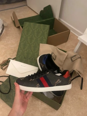 Gucci Ace sneakers  - Säljer dessa Gucci skor som aldrig vart använda. Däremot har de lite gröna fläckar (se bild) som jag antar är från själva boxen. Men borde gå att få bort med någon medel. Allt medföljer som är med på bilderna! Skorna är en present så kan inte lova äktehet. Storlek 42/43