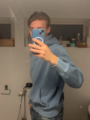 Blå hoodie från Polo Ralph Lauren - Säljer en snygg ljusblå hoodie från Polo Ralph Lauren med klassisk logga broderad på bröstet. Hoodien har huva med dragsko, ribbade muddar och en stor magficka. Perfekt för dig som gillar stilren och avslappnad look.