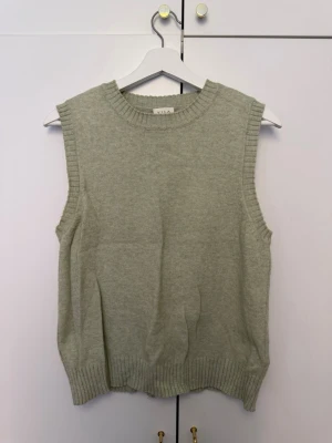 Ljusgrön stickad väst från Vila - Säljer en ljusgrön stickad väst från Vila. Västen har ribbade kanter vid halsringning, ärmhål och nederkant. Perfekt att styla över en skjorta eller t-shirt för en trendig lager-på-lager-look.
