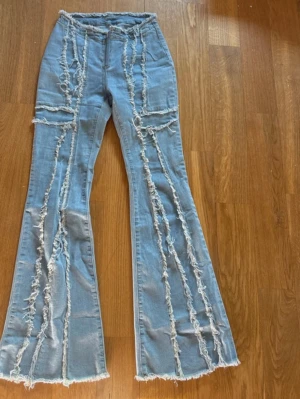 Ljusblåa bootcut jeans med fransar - Unika ljusblå jeans med bootcut-modell och råa fransade sömmar längs hela benen. Jeansen har hög midja och dragkedja framtill. Tillverkade i klassisk denim med coola slitningar för en trendig look.