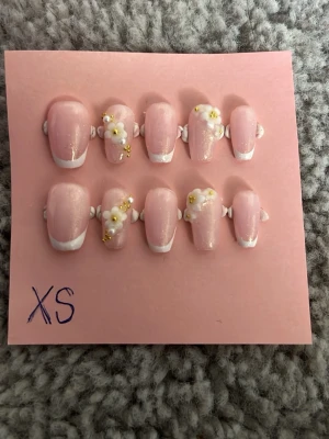 Press-on naglar - Snygga press-on naglar i ljusrosa med vit fransk tipp och skimrande glitter. Två naglar har 3D-blommor, pärlor och guldfärgade detaljer. Perfekt för dig som vill ha en elegant och kreativ look. Det ingår en buffer och ett nagellimm!!!!!