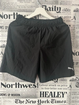 Svarta träningsshorts från Puma - Säljer ett par svarta träningsshorts från Puma med elastisk midja och klassisk logga på benet. Shortsen är tillverkade i ett lätt och snabbtorkande syntetmaterial, perfekta för gymmet eller löprundan. Se måttet på bilderna. 