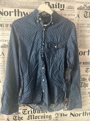 Blå skjorta med stjärnmönster - Snygg blå skjorta med små vita stjärnor, klassisk button-down krage och bröstficka med knapp. Skjortan har vita knappar och är tillverkad i ett mjukt bomullstyg. Perfekt för dig som gillar en avslappnad men ändå stilren look. Se måttet på bilderna, den är aldrig använd så helt ny bara utan prislapp då jag fick den i present. 