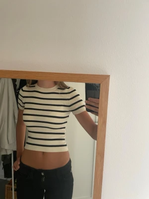 Randig ribbad topp med kort ärm - Säljer en ribbad topp med svart och vit randigt mönster. Modellen är croppad och har korta ärmar samt rund halsringning. Perfekt för dig som gillar en enkel men snygg stil. Materialet känns mjukt och stretchigt, troligen bomull eller polyester.