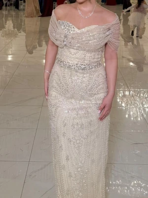 Champagnefärgad långklänning med pärlor - Säljer en elegant champagnefärgad långklänning med offshoulder och v-ringad design. Klänningen är dekorerad med pärlor och glittriga detaljer över hela tyget, samt har ett markerat midjeband med extra pärlor. Perfekt för bal eller fest, ger en lyxig och glamorös känsla. Den köptes för 2800kr från Tyskland men jag säljer den nu för 2000. Den är använd bara en gång. Priset går att diskutera. Storleken är 40 men passar perfekt för 38 också då jag har storlek 38. Skriv för fler bilder❤️