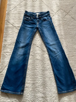 Blå bootcut jeans med dubbla knappar - Snygga mörkblå bootcutjeans från Gina Tricot, storlek 152. Använda en del men fortfarande fullt användbara. Några små lösa trådar men inga hål. Jeansen är sköna och snygga med bomullsmaterial. Riktig bra till en stilren vardags outfit.